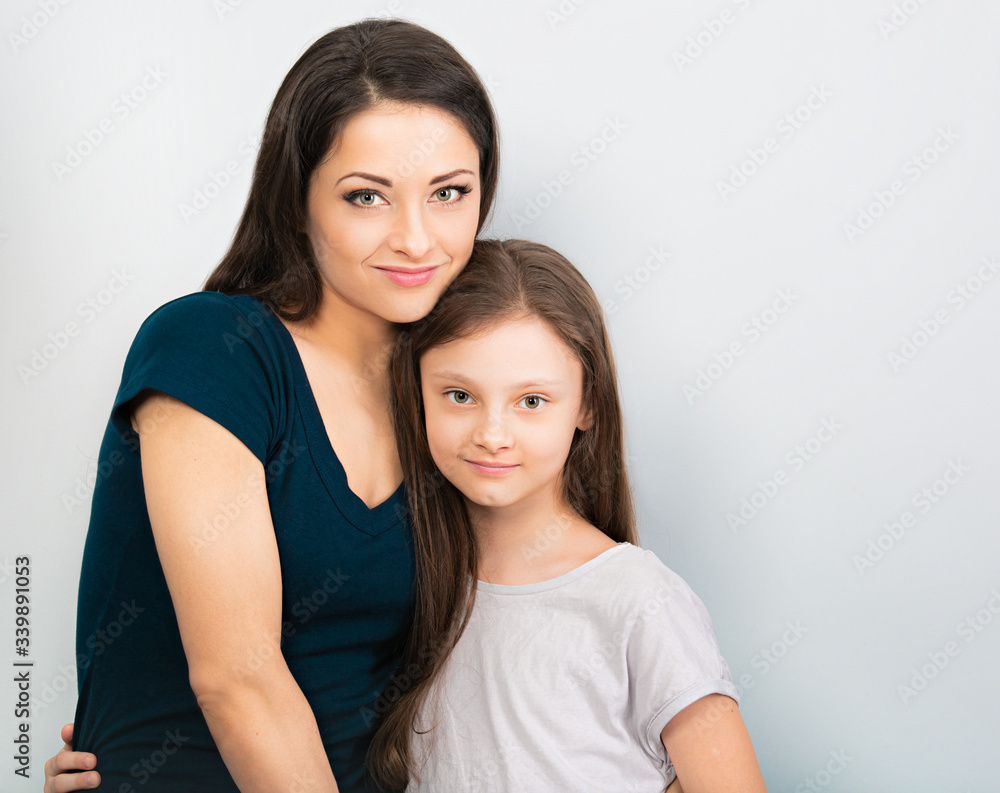 Beautiful calm mother and her smiling daughter hugging each other. Kid and young woman on blue copy space background. Closeup Beautiful calm mother and her smiling daughter hugging each other. Kid and young woman on blue copy space background. Closeup