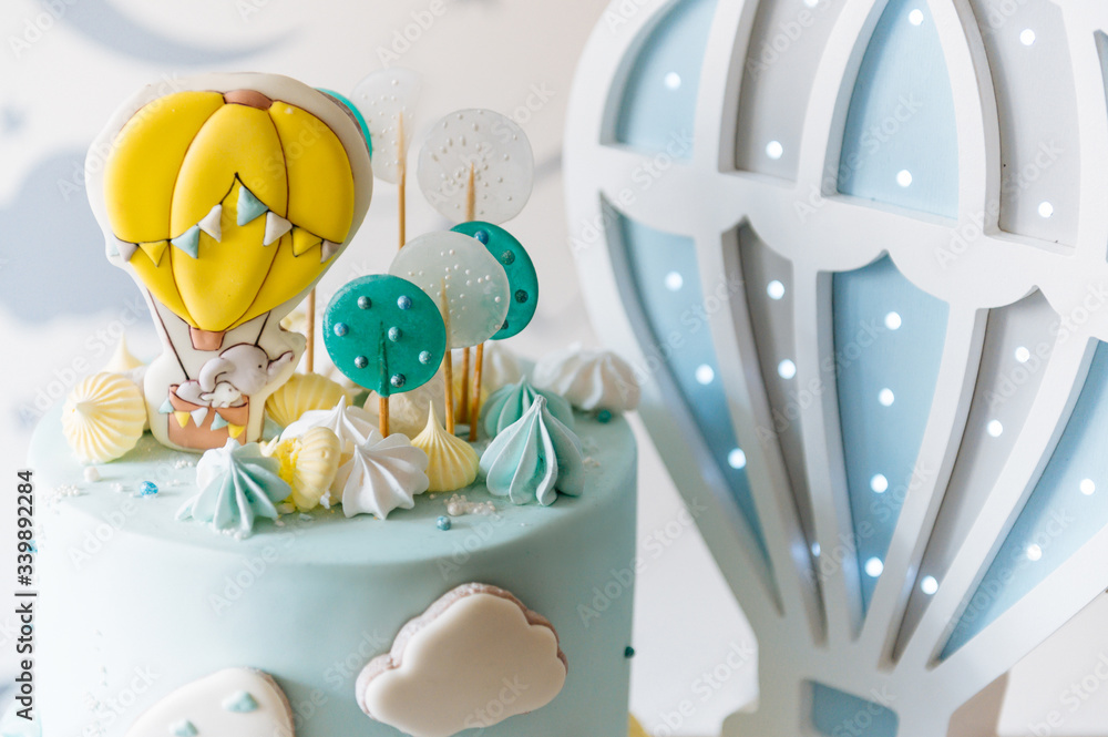 Children's first birthday cake, blue cake with clouds, meringue and balloons on the background of the children's room lights