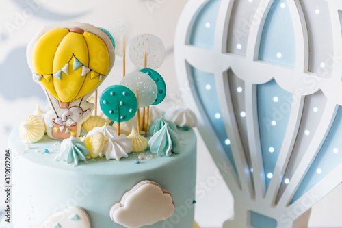 Children's first birthday cake, blue cake with clouds, meringue and balloons on the background of the children's room lights