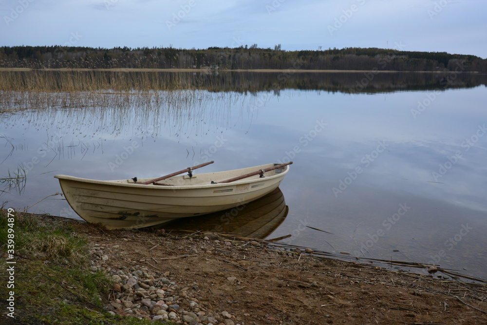 A rowing boat at the waterfront of mirror water surface with dark forest on the background. A rowing boat at the waterfront of mirror water surface with dark forest on the background.