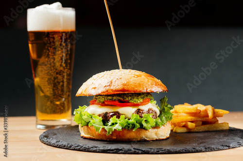 Beef burger with tomatos and fries on black plate with pint of lager beer on background. Junk food. Fastfood. Bodypositive. Food on quarantine from delivery. Photo for menu.
