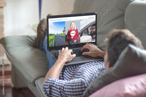 Man on the sofa using laptop with driving school online website on the screen