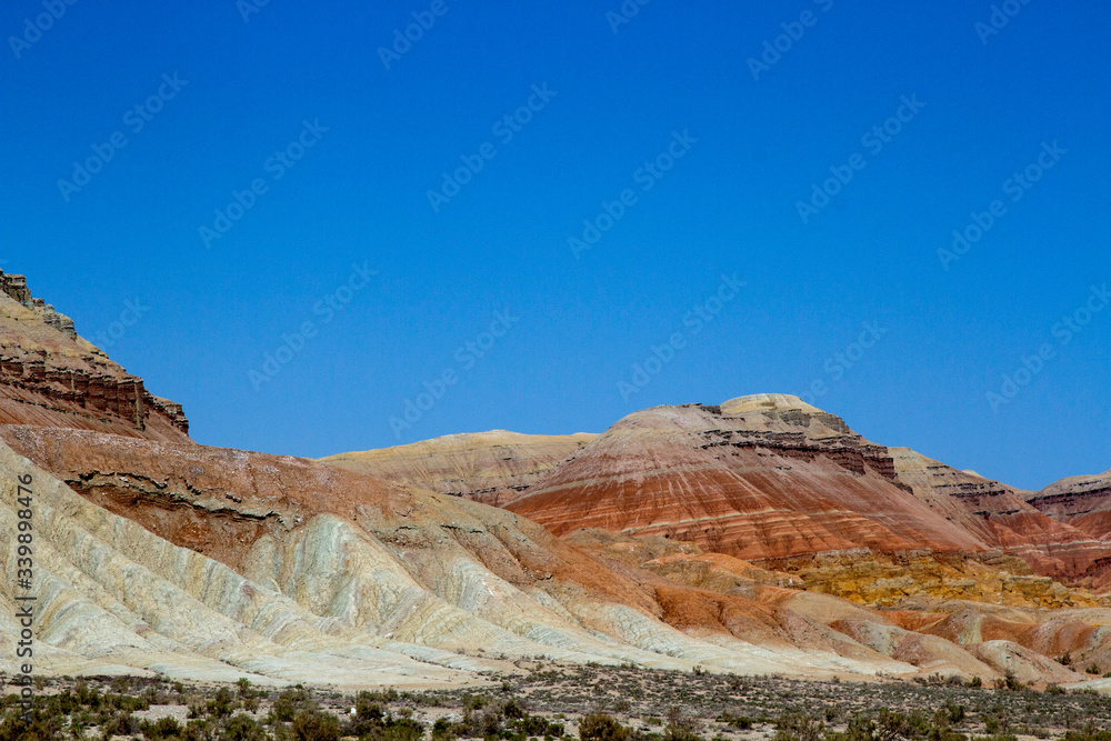 Colored, layered Aktau mountains in Kazakhstan among saxaul bushes. Above is a space for text. Colored, layered Aktau mountains in Kazakhstan among saxaul bushes. Above is a space for text.