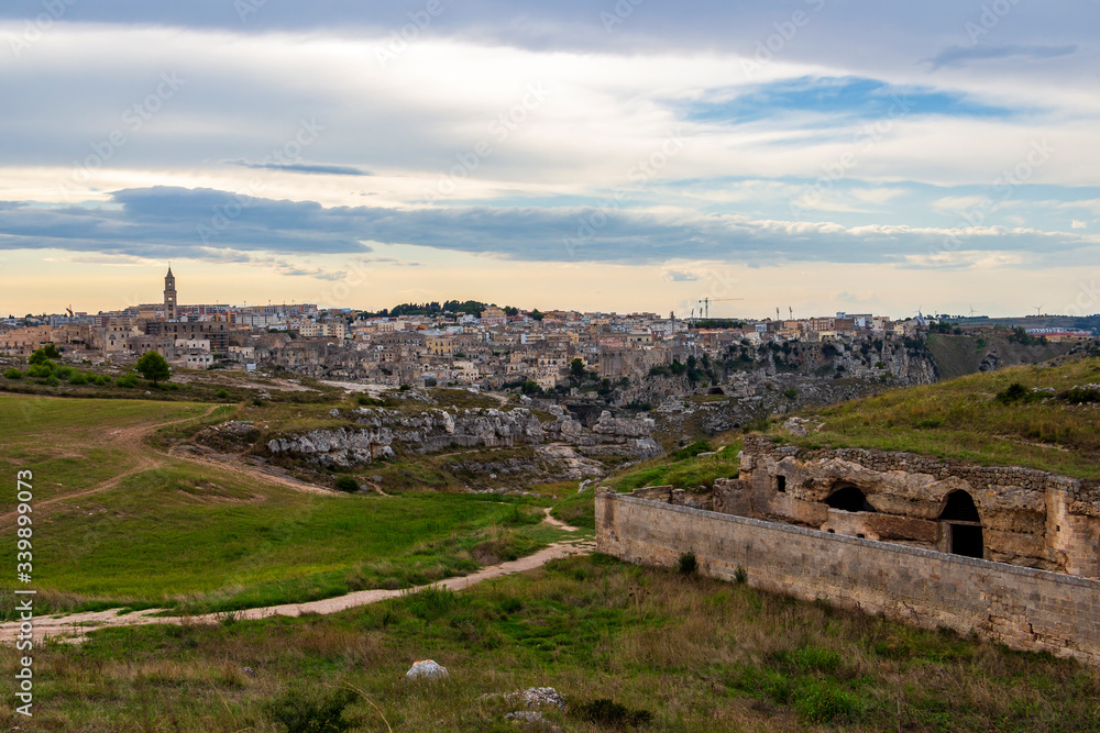 Parco della Murgia Materana or Park of the Rupestrian Churches of Matera with ancient architecture, distant panoramic view of Matera in the backgrond. Province of Matera, Basilicata Region, Italy at s