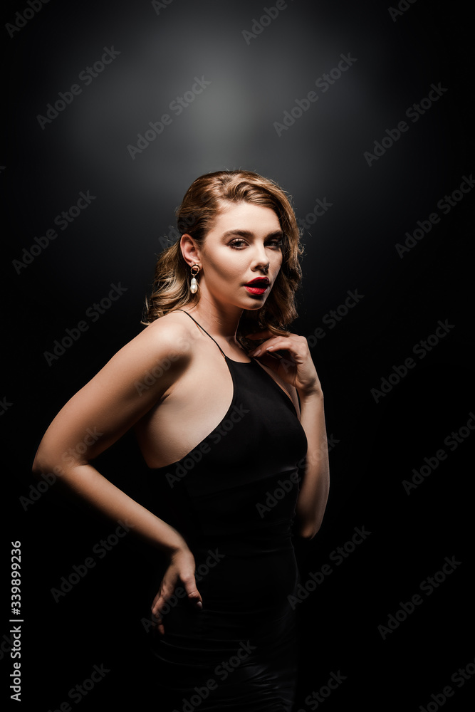sexy, elegant woman looking at camera while posing with hand on hip on black background sexy, elegant woman looking at camera while posing with hand on hip on black background