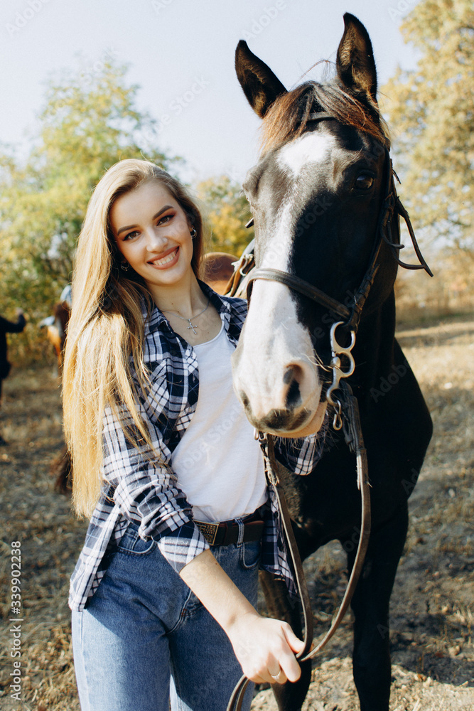 Obraz premium Portrait of beautiful young woman smiling and standing by horse in countryside. 