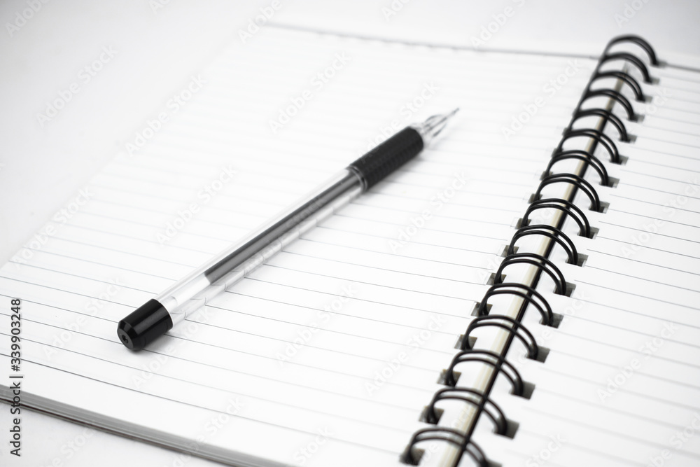 Single black colored pen placed on top of a simple open white paper diary Single black colored pen placed on top of a simple open white paper diary