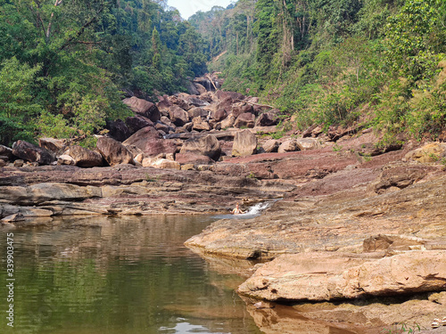 Young female traveler swimming in the dry waterfall. Big rocks with green forest in the jungles.