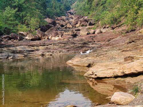 Young female traveler swimming in the dry waterfall. Big rocks with green forest in the jungles.