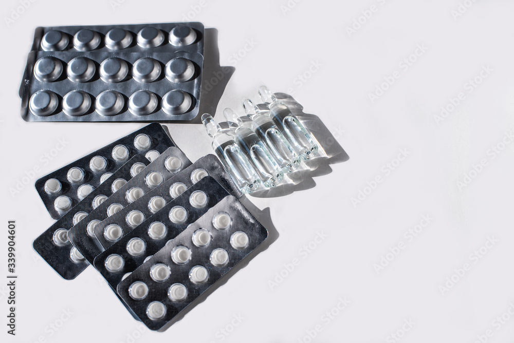 Different medicines: white plain breakable tablets in transparent sticks, in metal non-trasparent sticks and ampuls with anti-virus vaccine on white background. Copy space. Different medicines: white plain breakable tablets in transparent sticks, in metal non-trasparent sticks and ampuls with anti-virus vaccine on white background. Copy space.