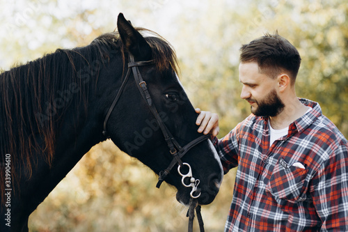 Portrait of young man standing by horse in countryside. 