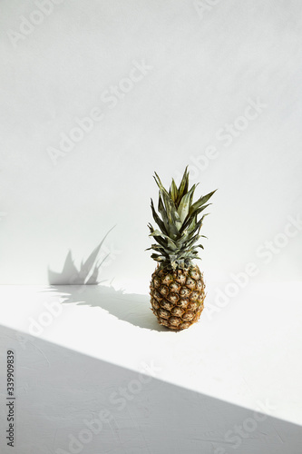 
Ripe tropical pineapple with green leaves and shadow play on a white background.