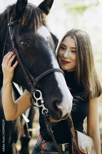 Portrait of beautiful young woman smiling and standing by horse in countryside. 