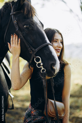 Beautiful stylish brunette woman near horse on ranch. Smiling girl hugging a horse. Human and animals relationship concept