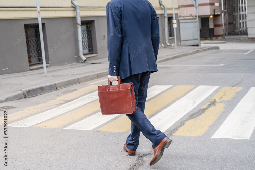 Alone middle-aged gray-haired businessman in a blue suit with briefcase laughing while calling by phone walks on the crosswalk on the city street. Alone middle-aged gray-haired businessman in a blue suit with briefcase laughing while calling by phone walks on the crosswalk on the city street.