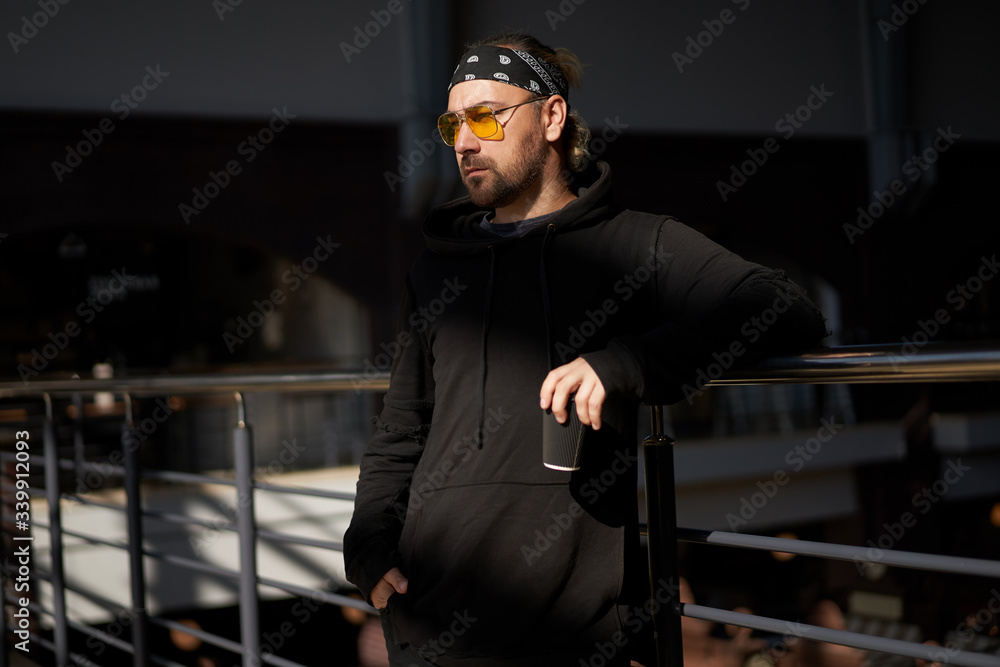 Handsome young unshaven man black hoodie and bandana stands Handsome young unshaven man black hoodie and bandana stands