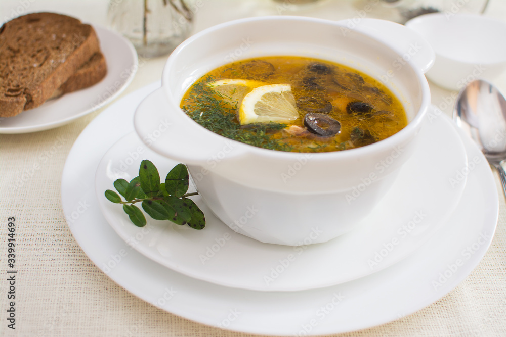 Traditional Russian meat soup solyanka with sausages, lemon and olives in a white ceramic bowl. Traditional Russian meat soup solyanka with sausages, lemon and olives in a white ceramic bowl.