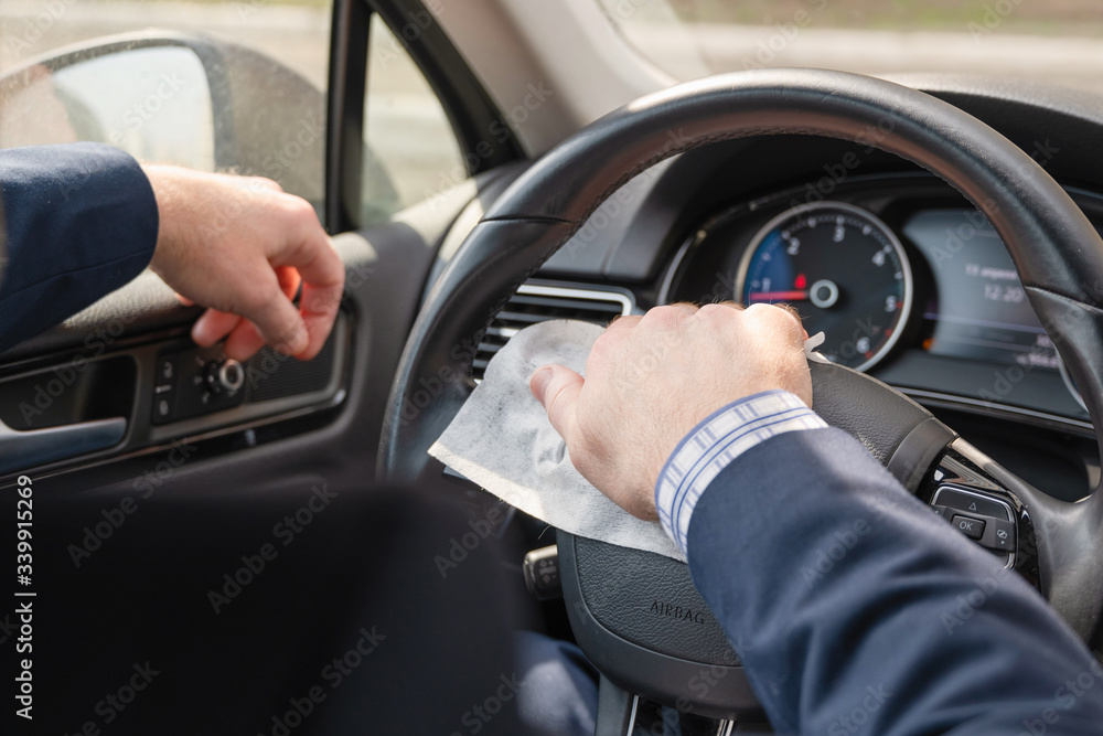 Naklejka premium Biznesmen w średnim wieku w niebieskim garniturze czyści kierownicę samochodu za pomocą antywirusowych, antybakteryjnych ściereczek (serwetki) w celu ochrony przed bakteriami i wirusami