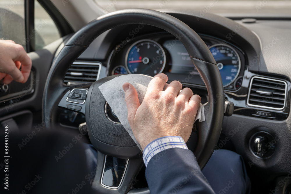Middle age businessman in a blue suit cleaning steering wheel of a car using antivirus antibacterial wet wipe (napkin) for protect himself from bacteria and virus