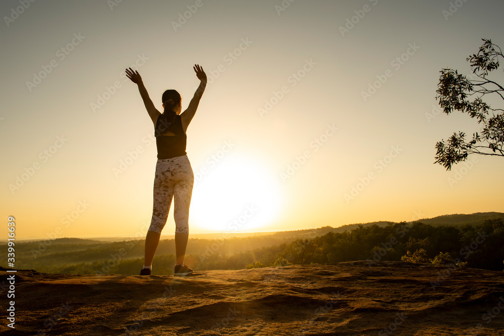 Young woman standing at the top of a mountain at sunrise.