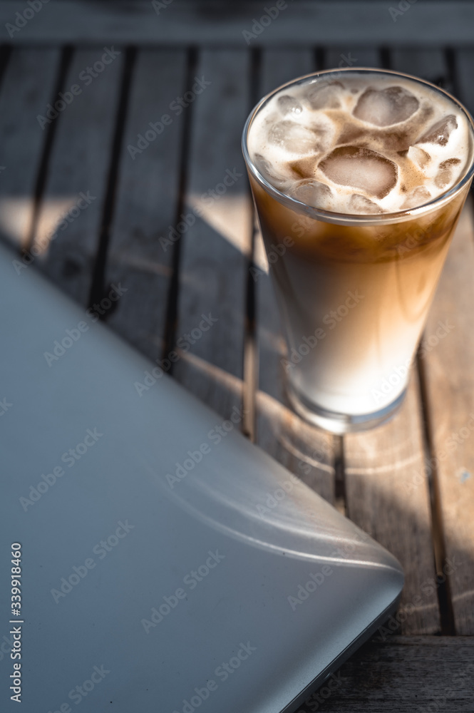 A cold Ice coffee on a sunny day on a wooden table with computer A cold Ice coffee on a sunny day on a wooden table with computer
