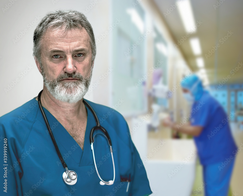 Portrait of a doctor in the hospital, in the background one of his colleagues is washing his hands Portrait of a doctor in the hospital, in the background one of his colleagues is washing his hands