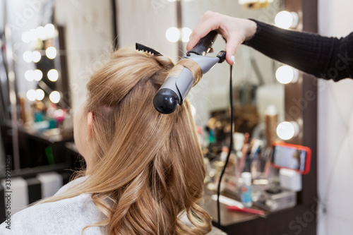 A blonde woman is wound a lock of hair on a curling iron in a professional beauty salon. Close-up.