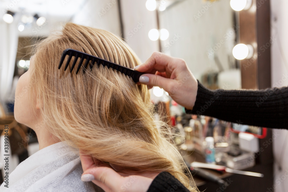 A blonde woman is combing her hair in a professional beauty salon. Beauty and care. Close-up. Back view. A blonde woman is combing her hair in a professional beauty salon. Beauty and care. Close-up. Back view.