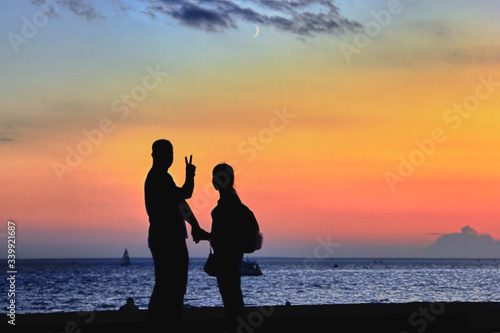 silhouettes of a young couple in a pink sunset with the moon on the background of the sea