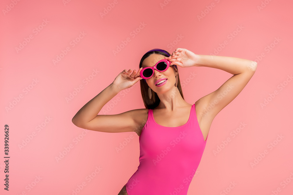 Woman smiling and touching sunglasses isolated on pink Woman smiling and touching sunglasses isolated on pink