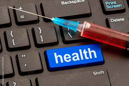 Syringe with vaccine on the computer keyboard with HEALTH button