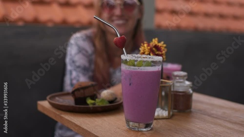 Close-up of waitress holding berry smoothie, serving it to cafe visitors.  Camera slowly moves over female hands with drink and the table with healthy sweets.
