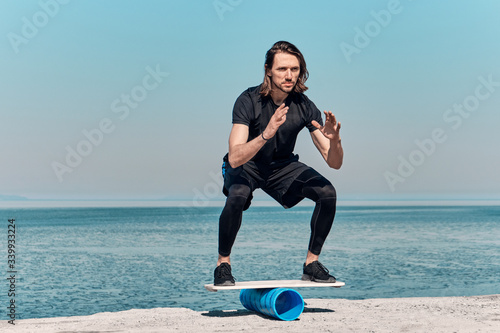 Closeup Of Healthy Handsome Active Man With Fit Muscular Body keeping balance on the wooden board against the background of sea on summer day