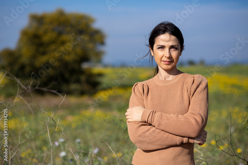 ragazza con maglione colo cachi guarda seria , sullo sfondo campagna e un prato naturale verde e giallo con cielo blu. photo