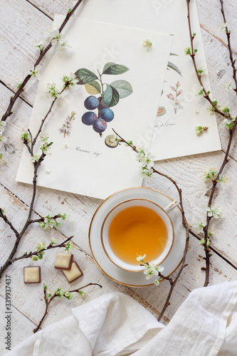 Bright spring flat lay with a cup of tea, some prints and blooming plum tree branches