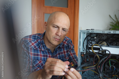 A man is fixing a computer. It connects parts in a disassembled system unit.