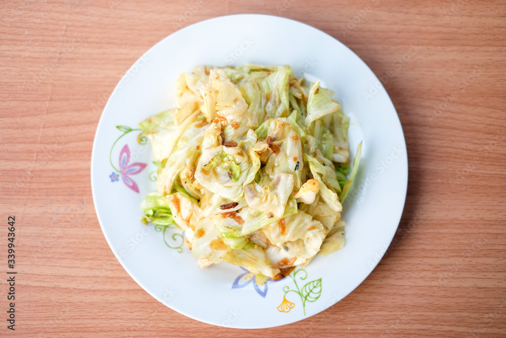 The hot stir fried cabbage with fish sauce serve on white dish set on brown table - homemade food concept.