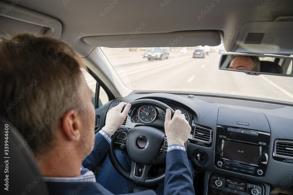 Middle age businessman in a blue suit and rubber gloves for protect himself from bacteria and virus driving a car. Coronavirus. Pandemic. Middle age businessman in a blue suit and rubber gloves for protect himself from bacteria and virus driving a car. Coronavirus. Pandemic.