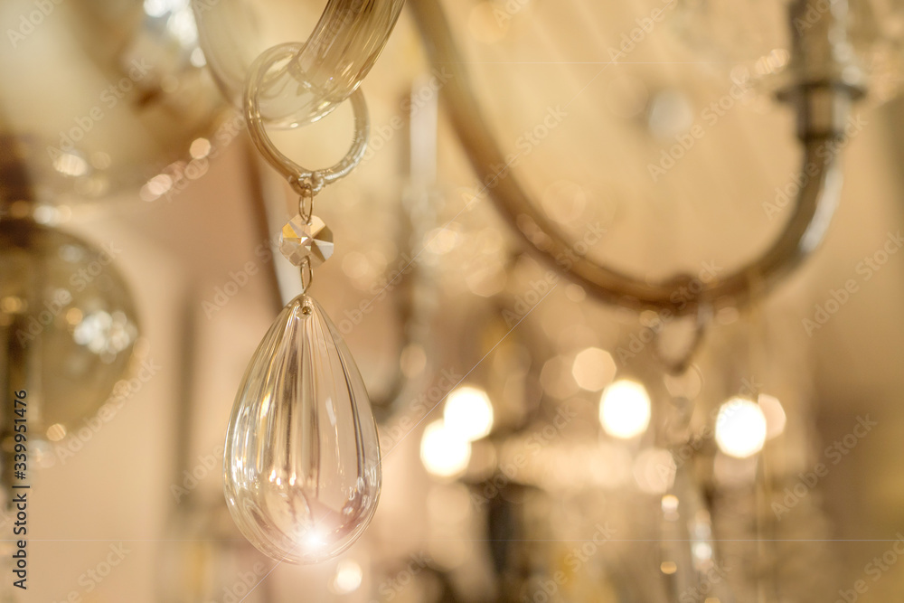 A photo of the crystal decor of a drop hanging on the transparent glass armature of the ceiling chandelier in the interior. Concept of luxury design. Close up. Soft warm filter, selective focus.