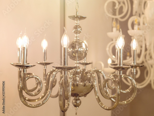 The image of a bright chandelier with metal chrome fixtures and shades in the form of candles. The concept of the classical style in the interior. Close up. Soft warm filter  selective focus.
