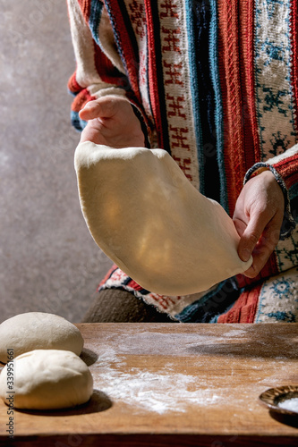 Woman in knitted sweater cooking italian pizza napolitana. Pulling fresh homemade wheat dough on wooden kitchen table. Home baking. photo