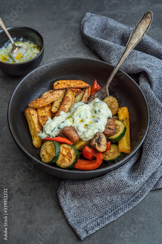 Teller mit Grillgemüse, Kartoffelspalten und Tzatziki auf einem dunkel Hintergrund