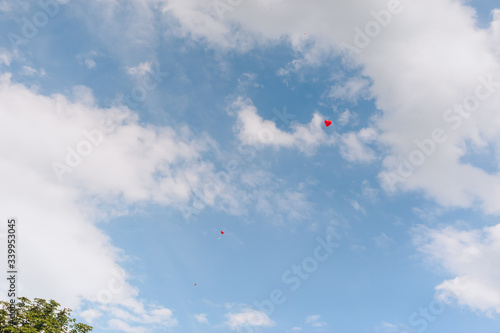 A red heart-shaped balloon flies against a blue sky with clouds. Photography, concept.