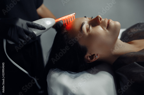Cosmetologist makes the procedure microcurrent therapy on the hair of a beautiful young woman in cosmetology salon. photo