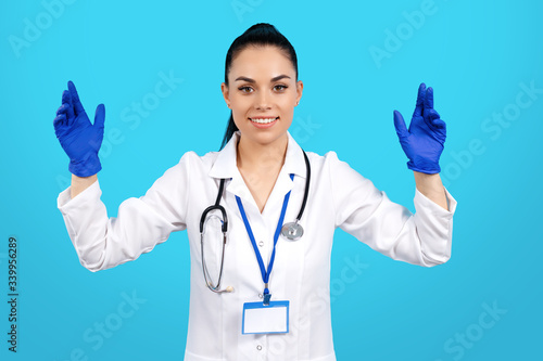 Portrait of pretty young woman doctor with stethoscope wearing gloves over blue background.