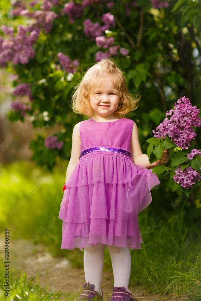 small girl in purple dress near bush of lilac