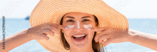 Beautiful young woman in hat is applying sunblock under her eyes and on her nose like Indian. Sun protection concept
