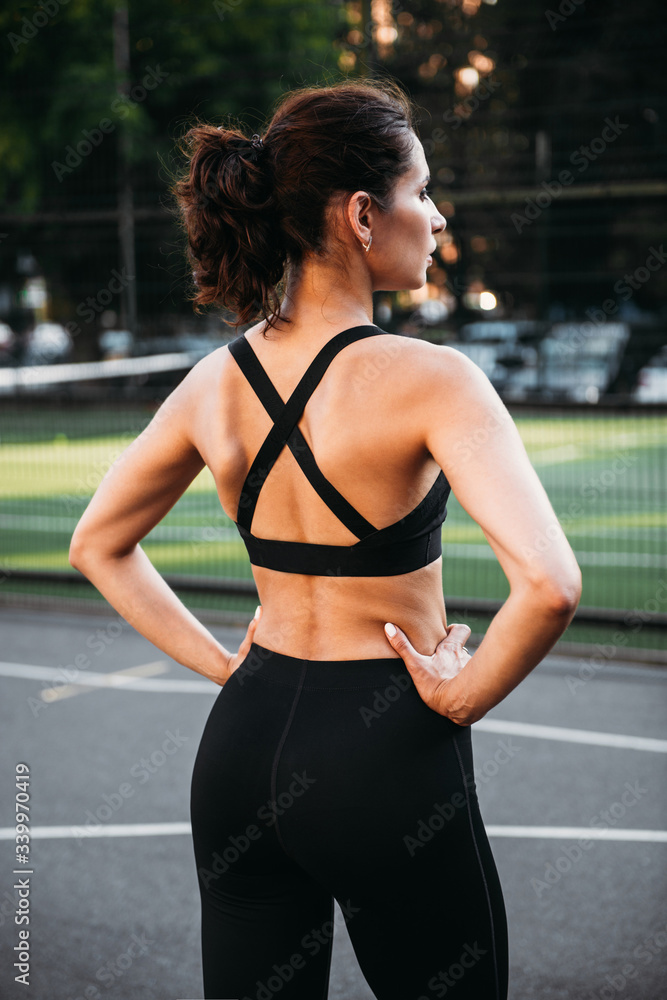 Beautiful sexy fitness young woman wearing black leggings and sport bra  standing at the court outside. Energetic fit caucasian dark hair girl  posing for the camera. Stock Photo | Adobe Stock