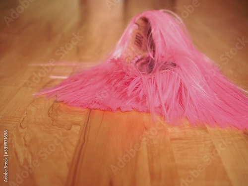 A girl in black shoes walks on a wooden floor and drops a pink wig on the floor. The concept of dressing up, freaks or party photo