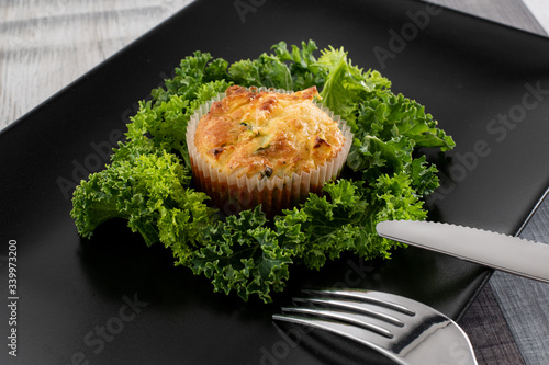 Freshly Baked Courgette and Tuna Muffins on a dark plate with kale. Proposal of serving the dish.